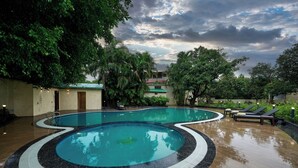 Una piscina de diseño curvo, rodeada de sillones de descanso y un entorno verde exuberante.