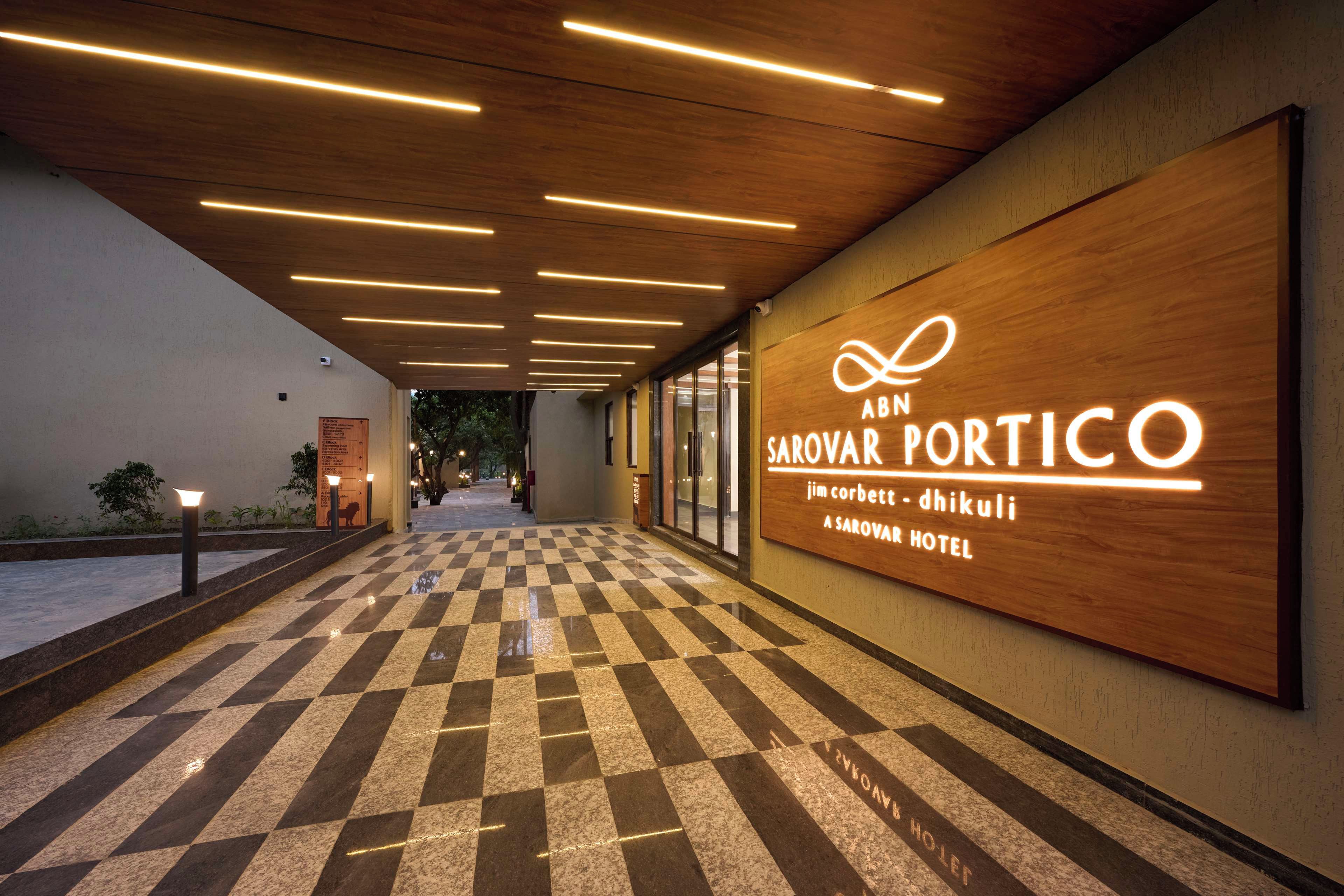A hotel corridor with a checkered floor, wooden ceiling panels, and a neon sign for ABN SAROVAR PORTICO.
