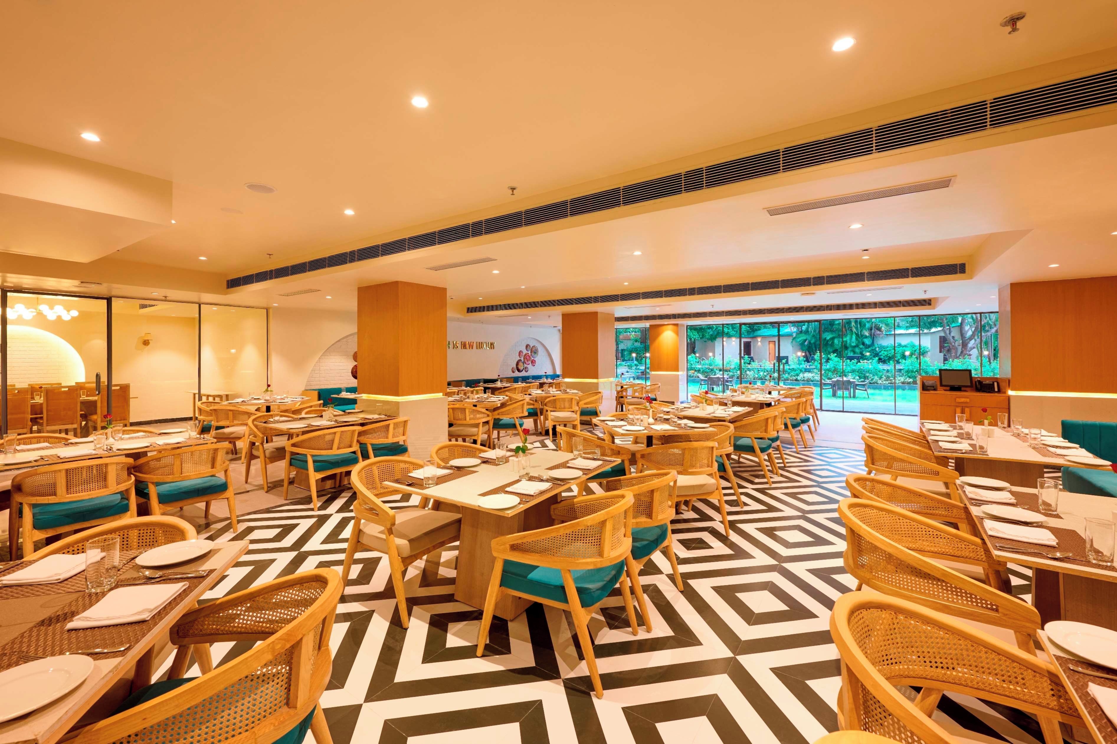 A spacious restaurant with multiple dining areas, including a central open space with tables and chairs, and a separate dining area with a view of the outdoors.