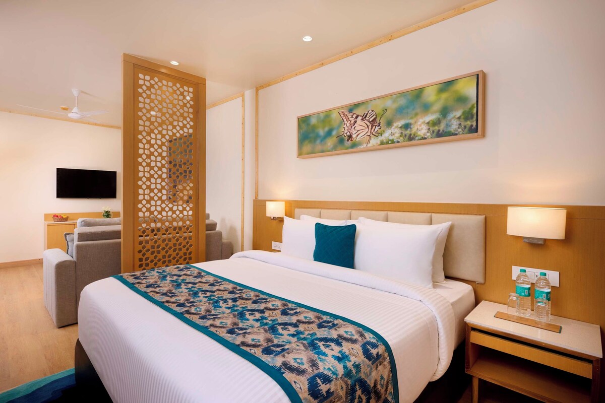 Una habitación de hotel con una cama, un escritorio, una silla, un televisor y un cuadro en la pared.