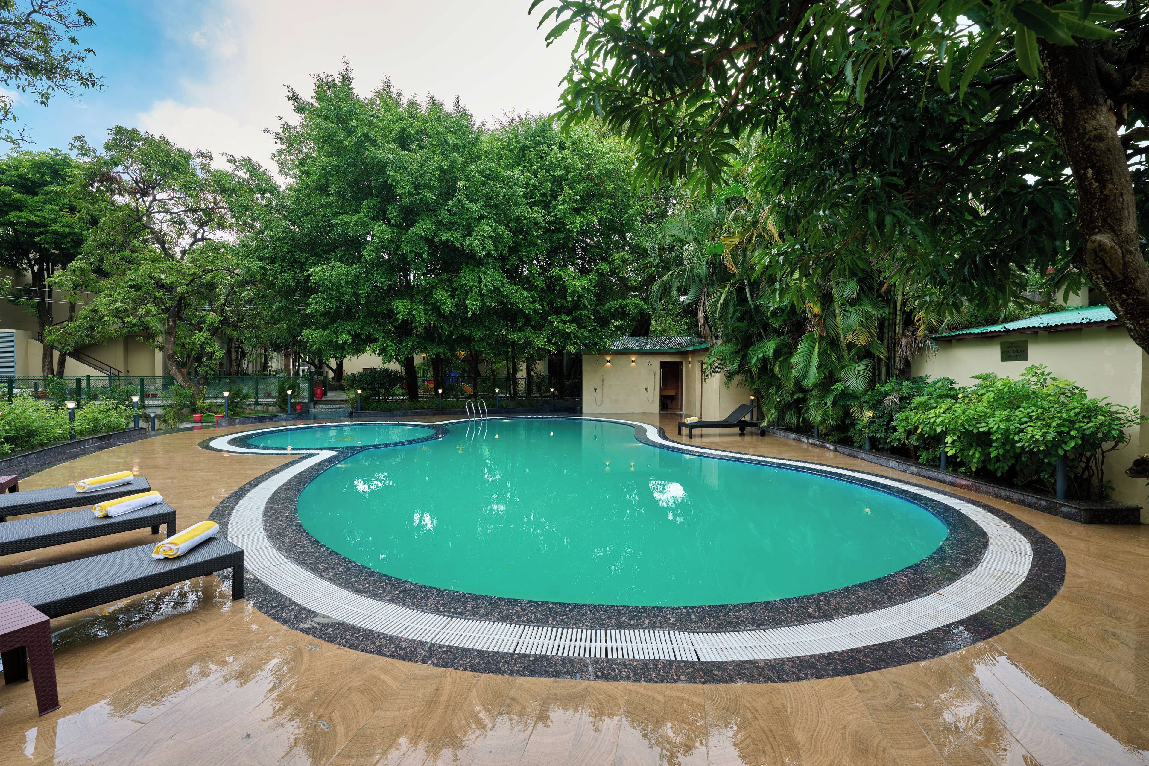 Una piscina dalla forma sinuosa, circondata da sdraio e un piccolo edificio, probabilmente un locale per i cambi o un deposito.