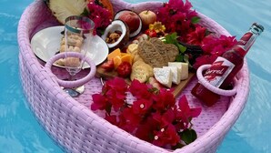 Uma cesta de vime em formato de coração, cheia de comida e bebidas, flutuando em uma piscina.