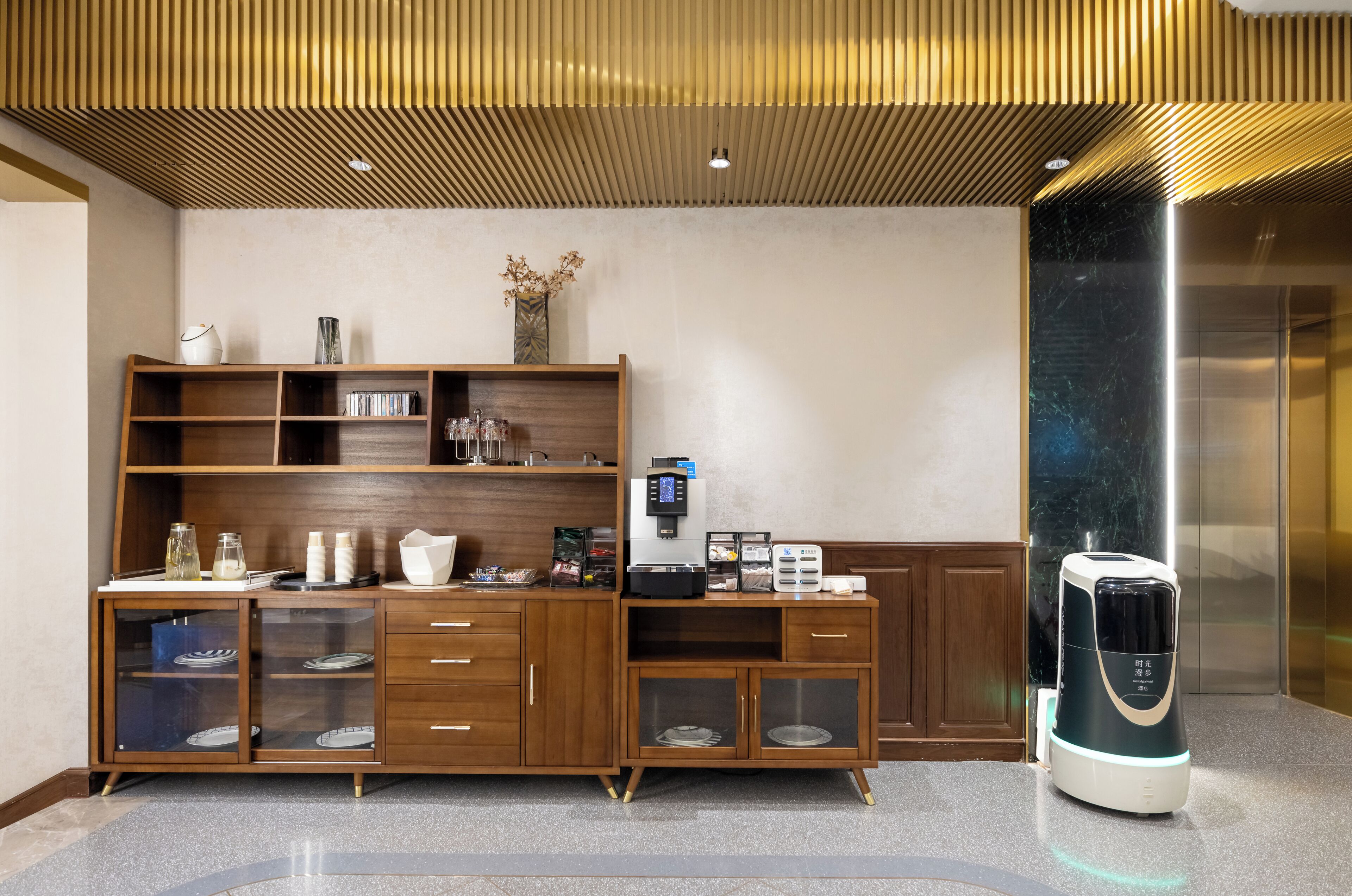 A modern hotel reception area with a wooden reception desk, a coffee machine, and a glass display cabinet.
