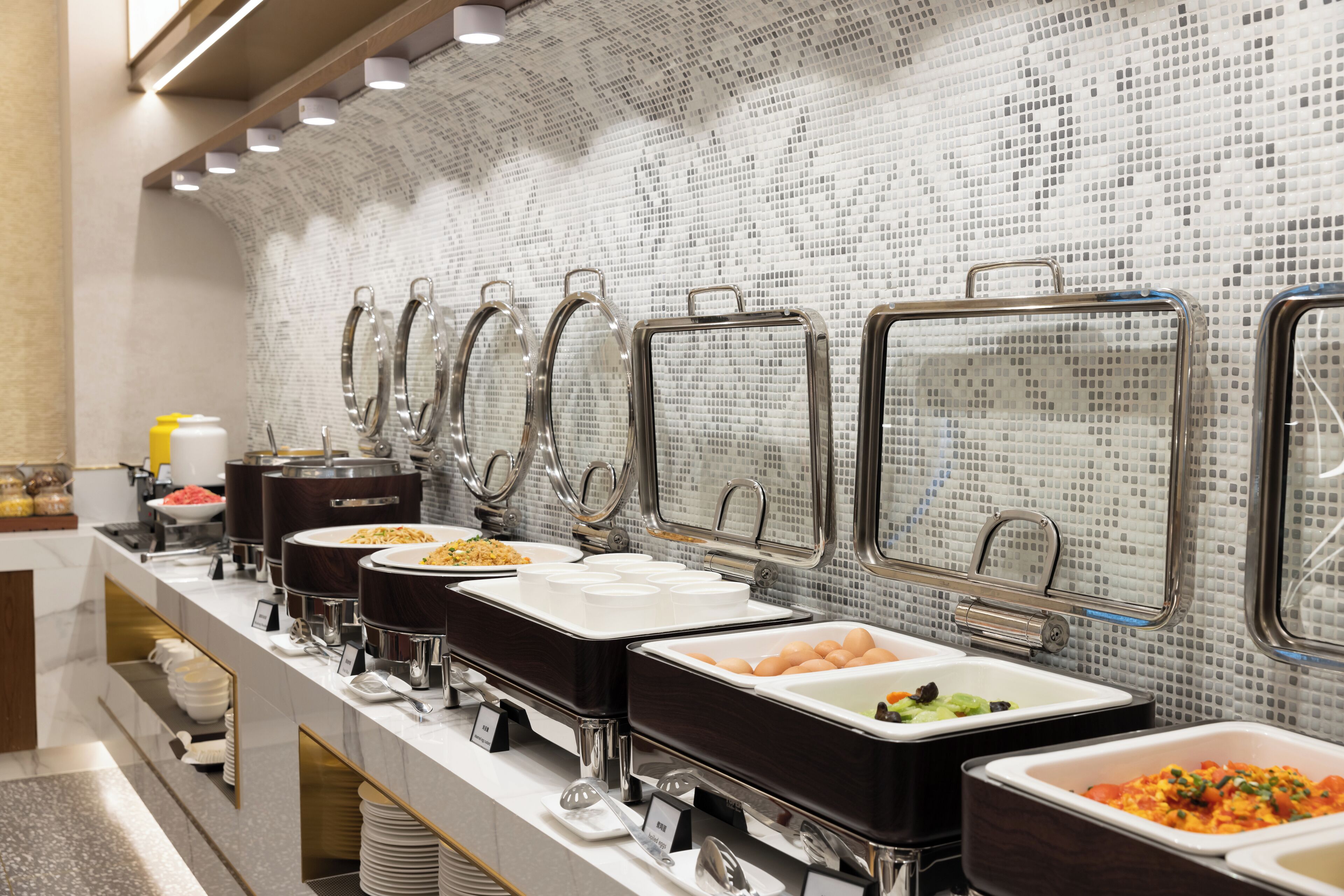 A buffet setup with multiple serving stations, each with a metal frame and a glass top.