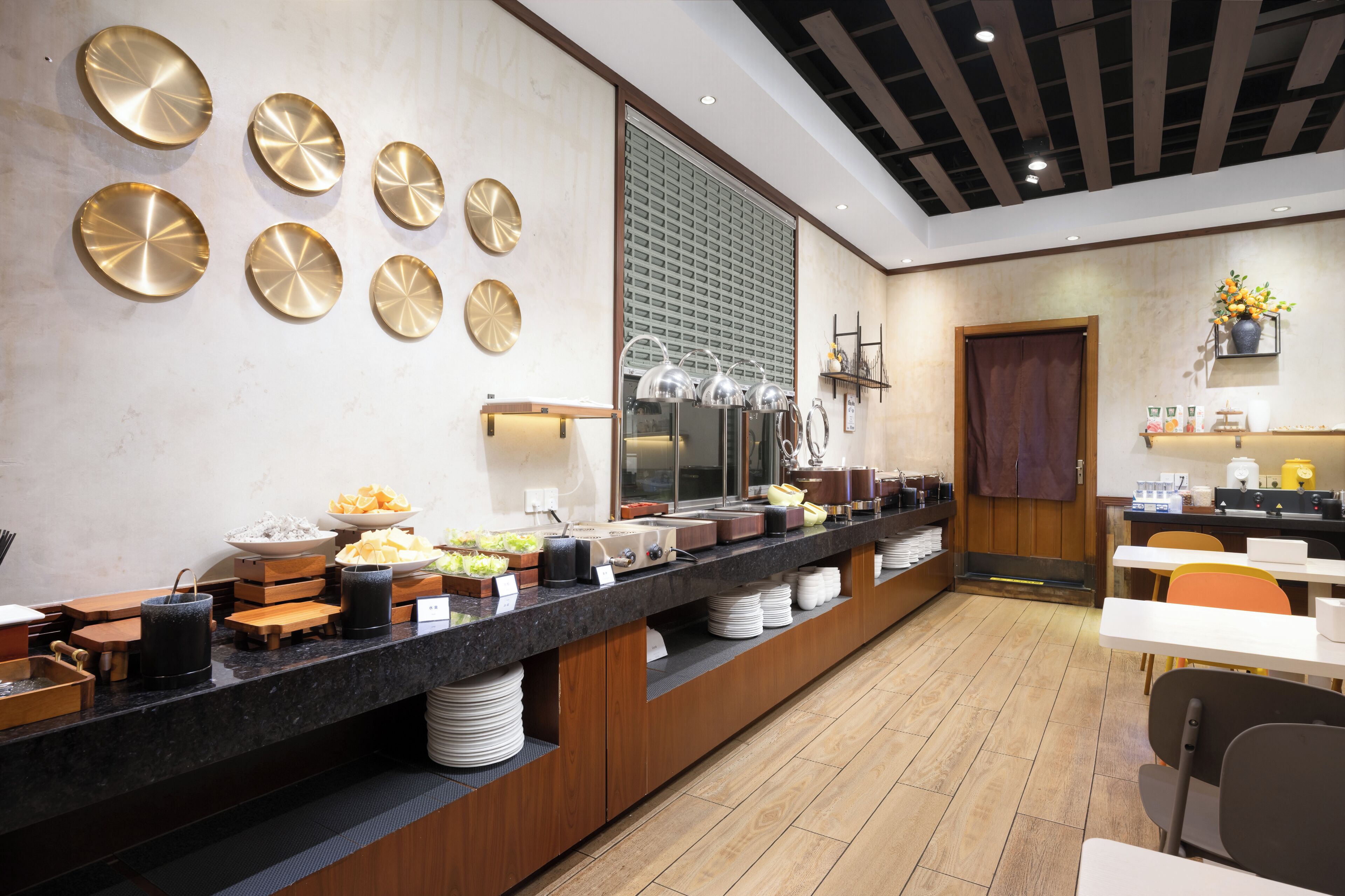 Uma área de buffet com um balcão extenso, diversos tipos de comida e um espaço de refeições com mesas e cadeiras.