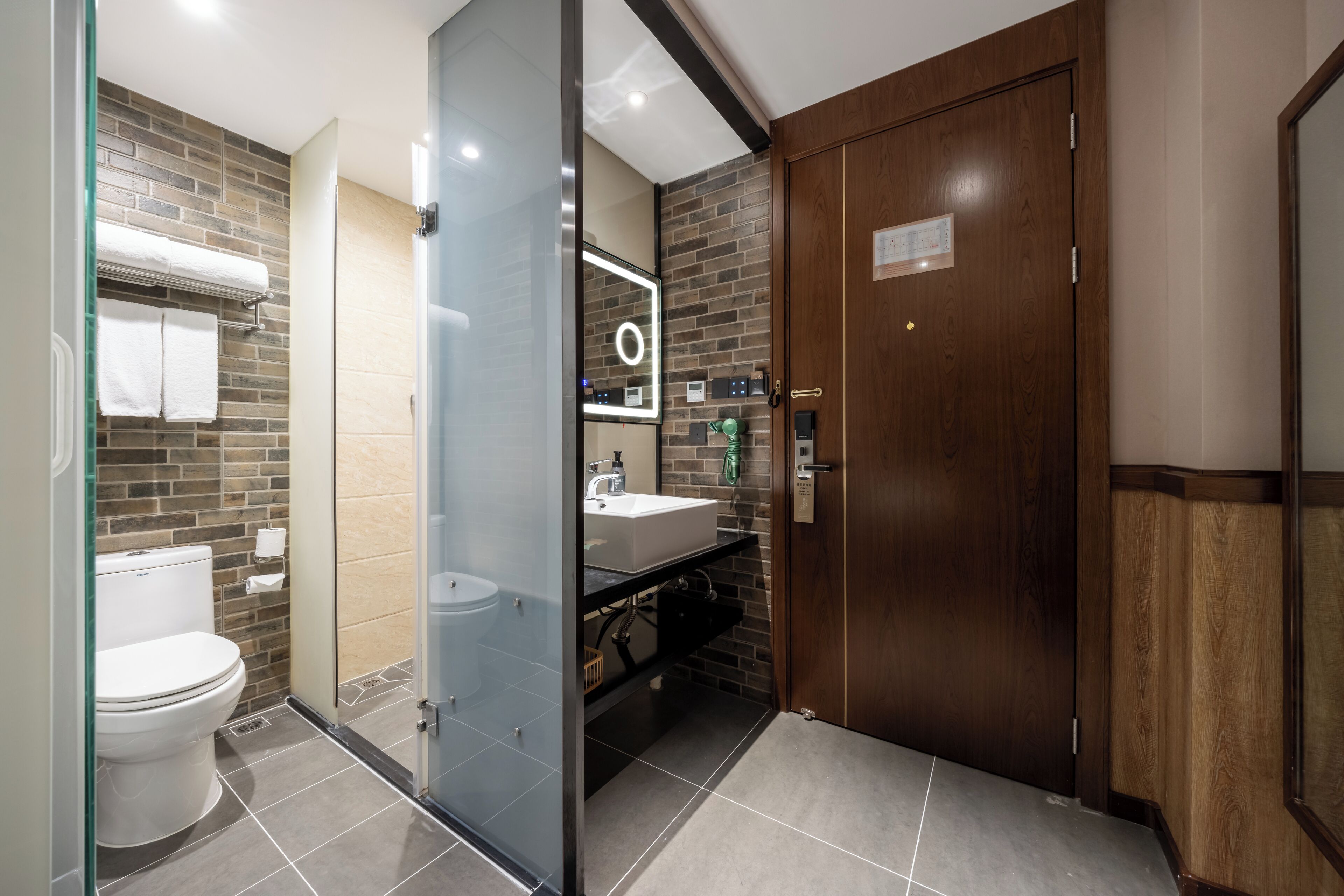 A modern bathroom with a glass partition, a wooden door, and a visible toilet.