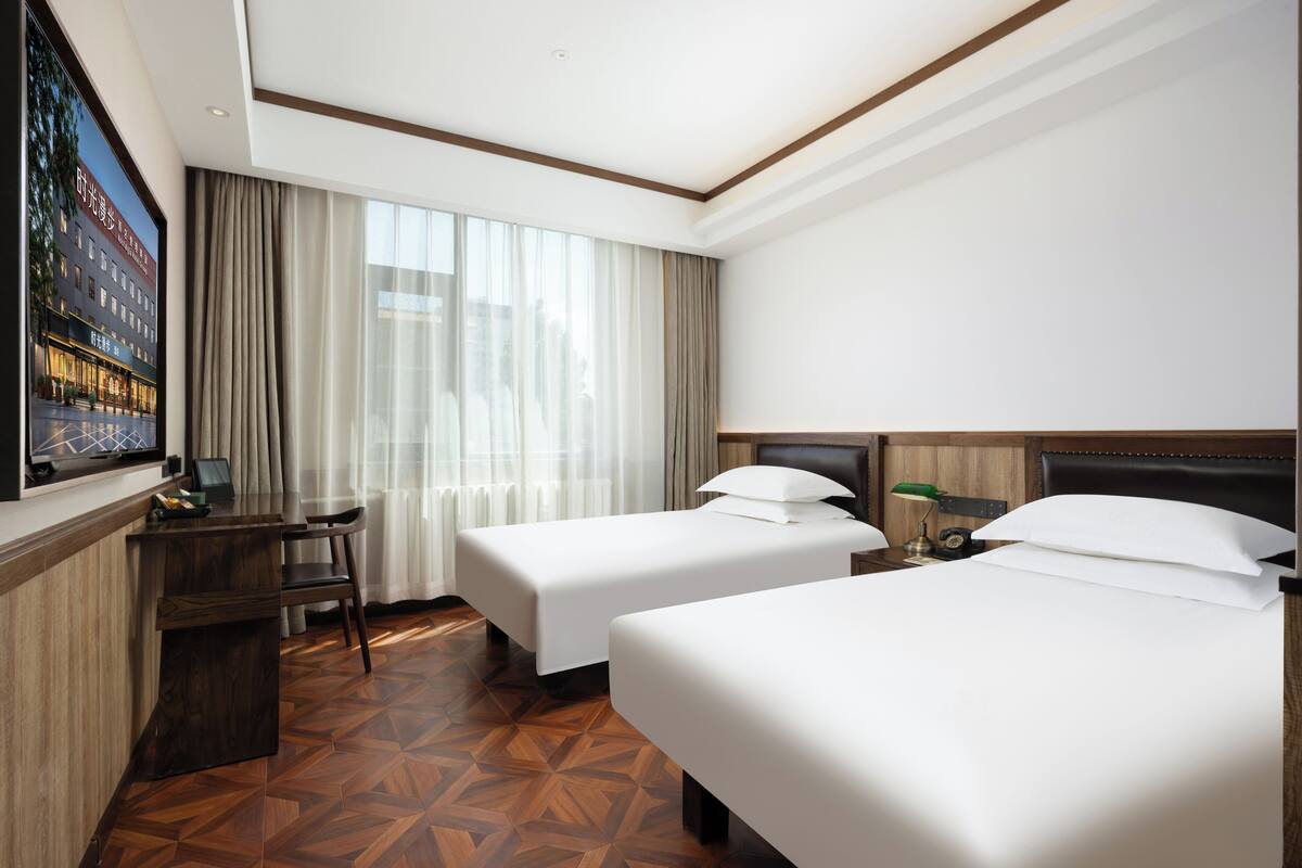 A hotel room with two beds, a desk, a chair, and a large window with curtains.