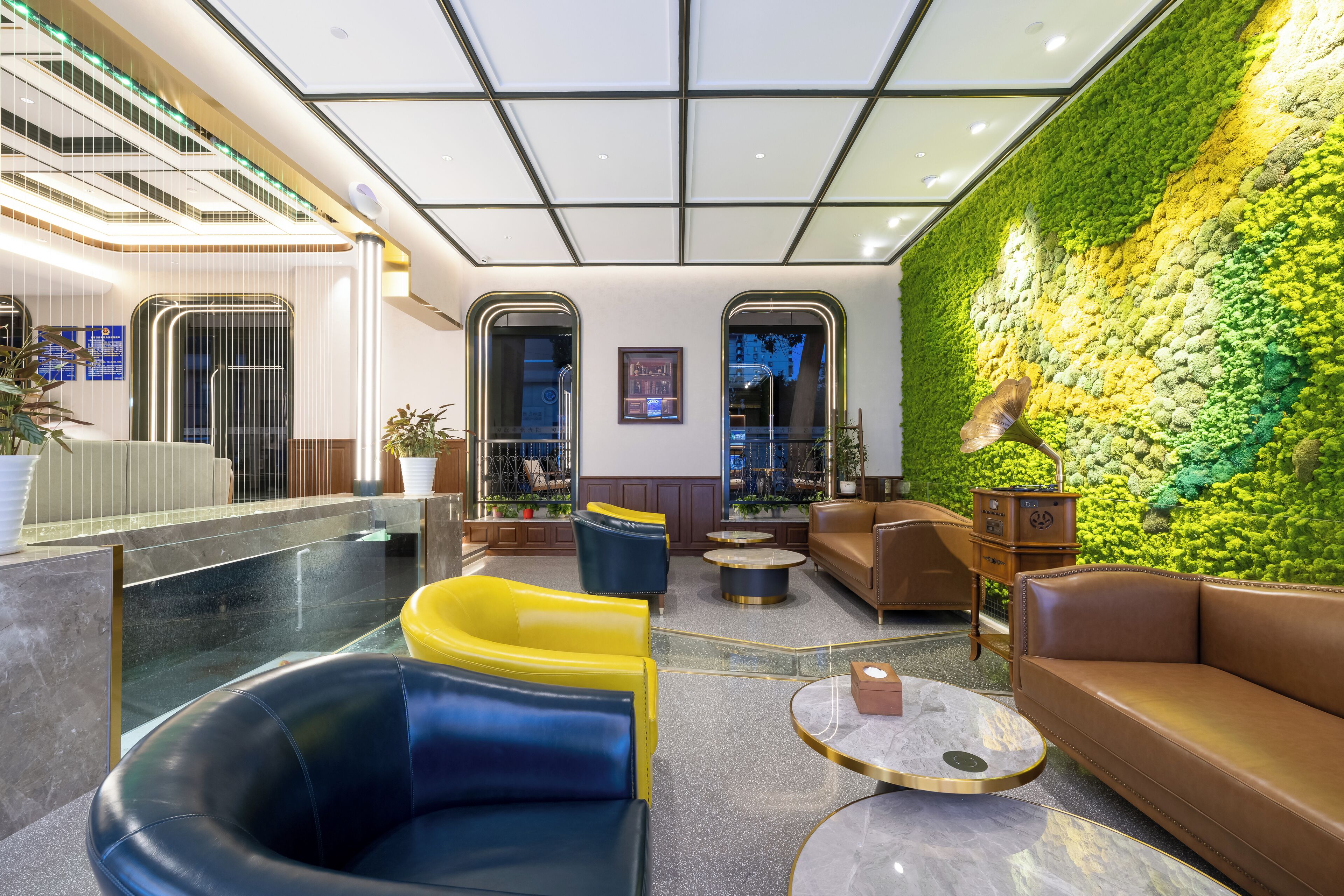 Un vestíbulo moderno con una pared verde, zonas de estar y una recepción.