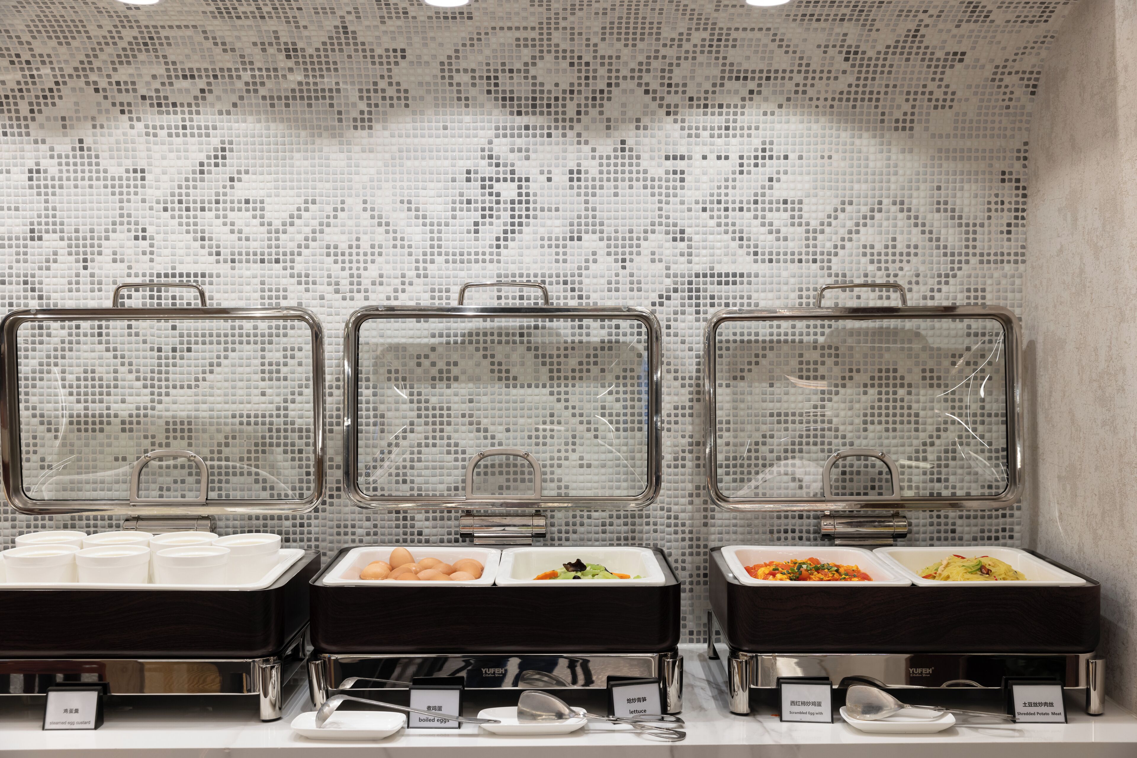 Ein Buffet mit drei Speisenausgabestationen, jede mit verschiedenen Speisen beschriftet.