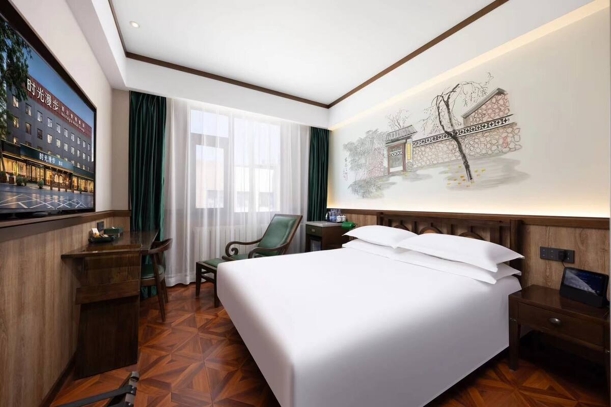 A hotel room with a large bed, a desk, a chair, a TV, and a wall with a mural.