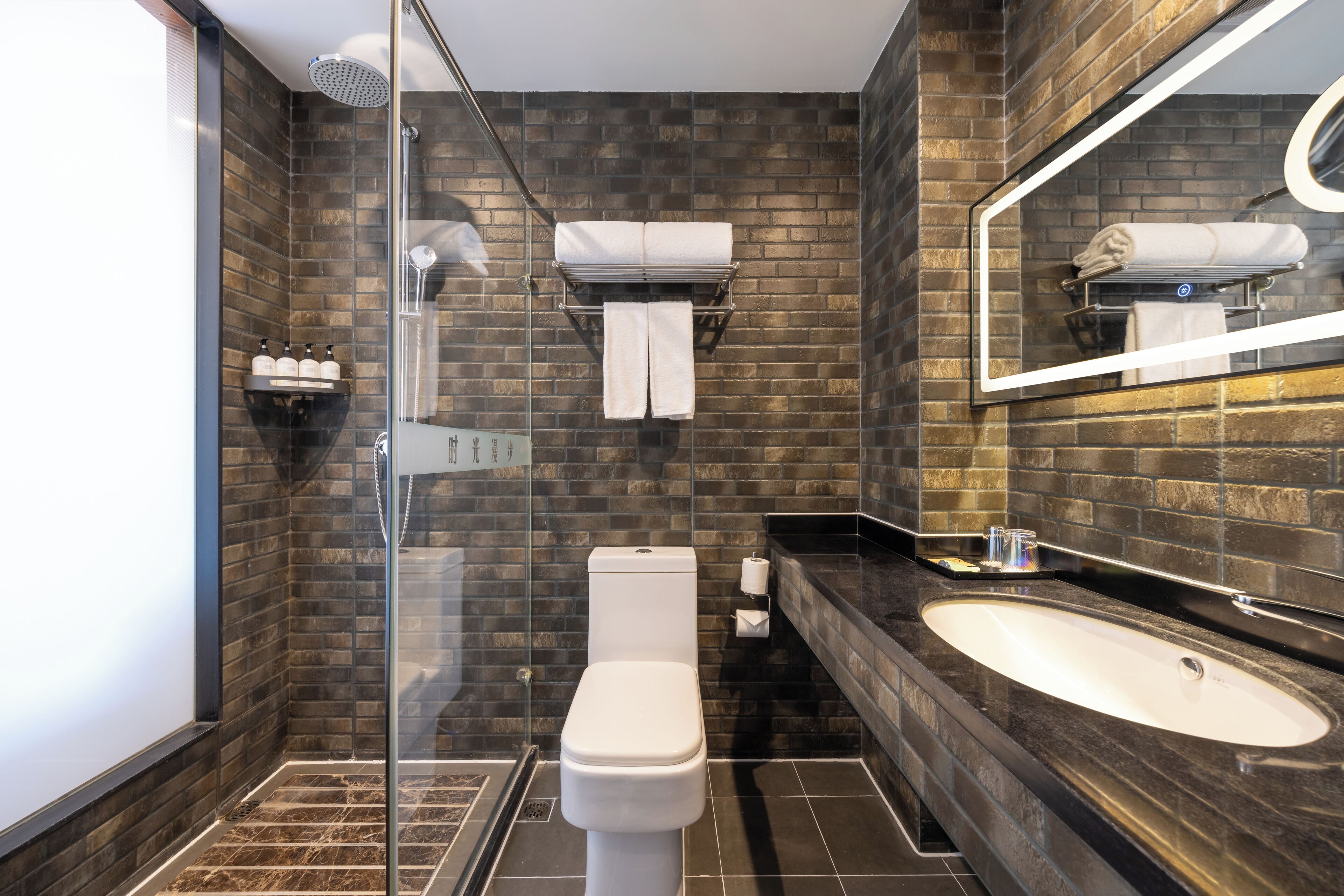 Un baño moderno con cabina de ducha de vidrio, inodoro blanco, lavabo de mármol oscuro y un espejo grande.