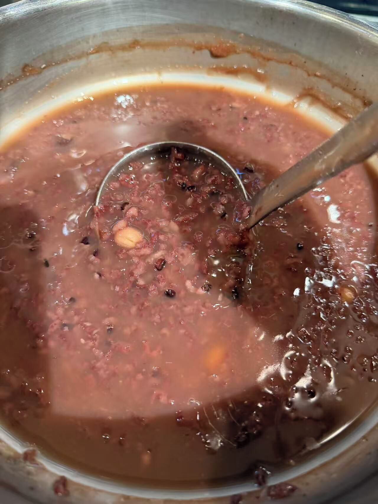A close-up of a pot with a thick, reddish-brown soup containing visible beans and spices.