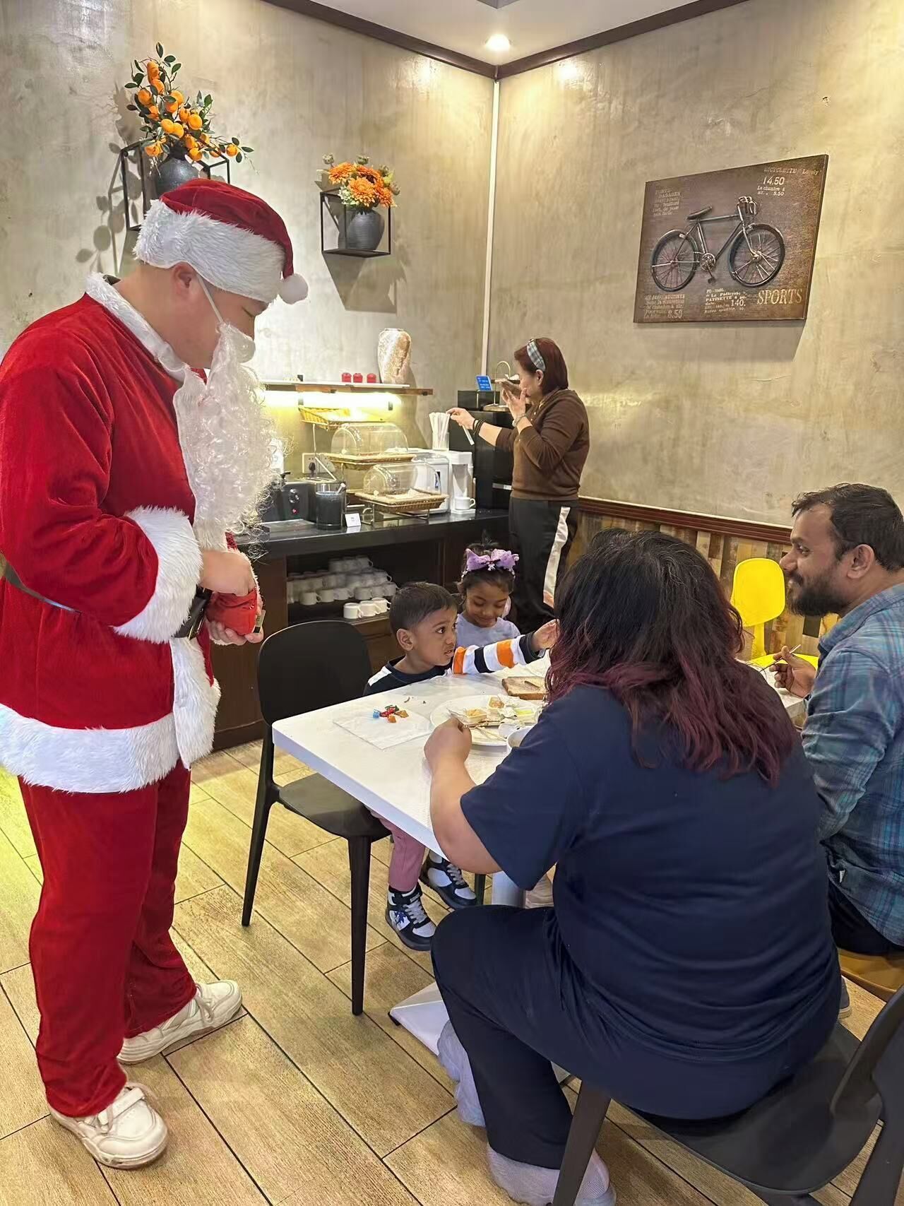 A dining area with a table set for a family meal, a person in a Santa costume, and a bicycle-themed wall decoration.