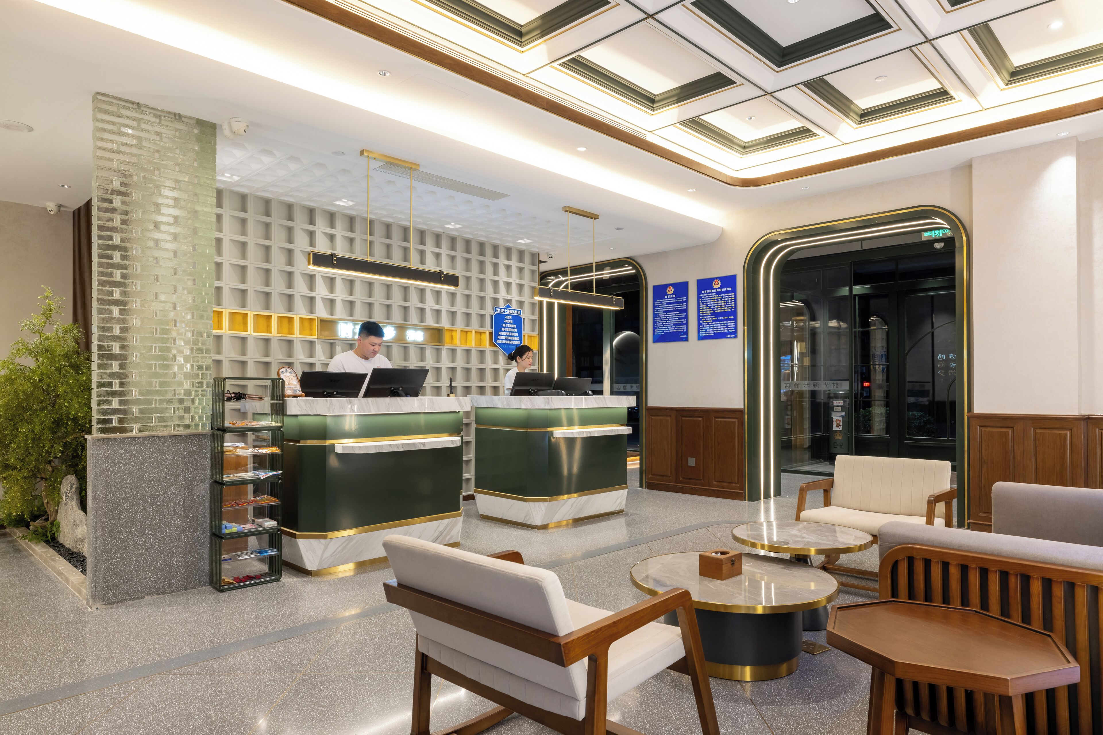 Un hall d’hôtel moderne comprenant un comptoir d’accueil, un espace salon et un ascenseur en verre.