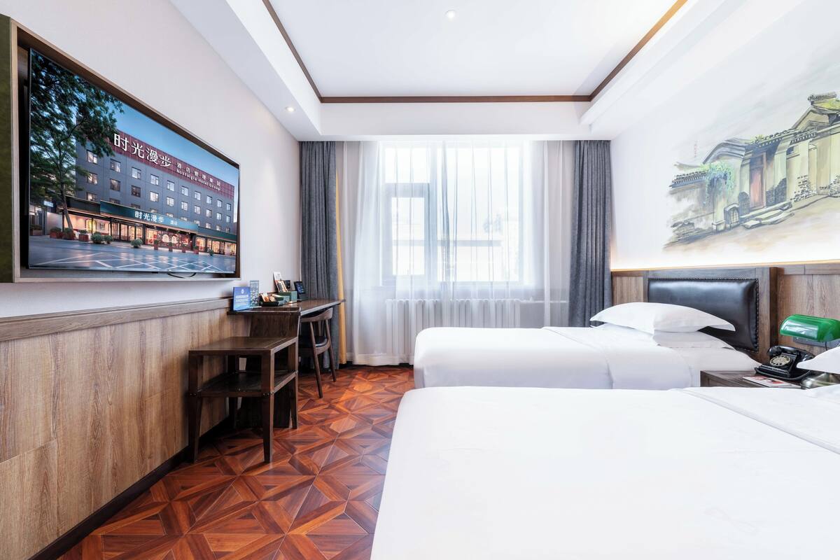 A hotel room with a large bed, a desk with a chair, a television mounted on the wall, and a window with curtains.