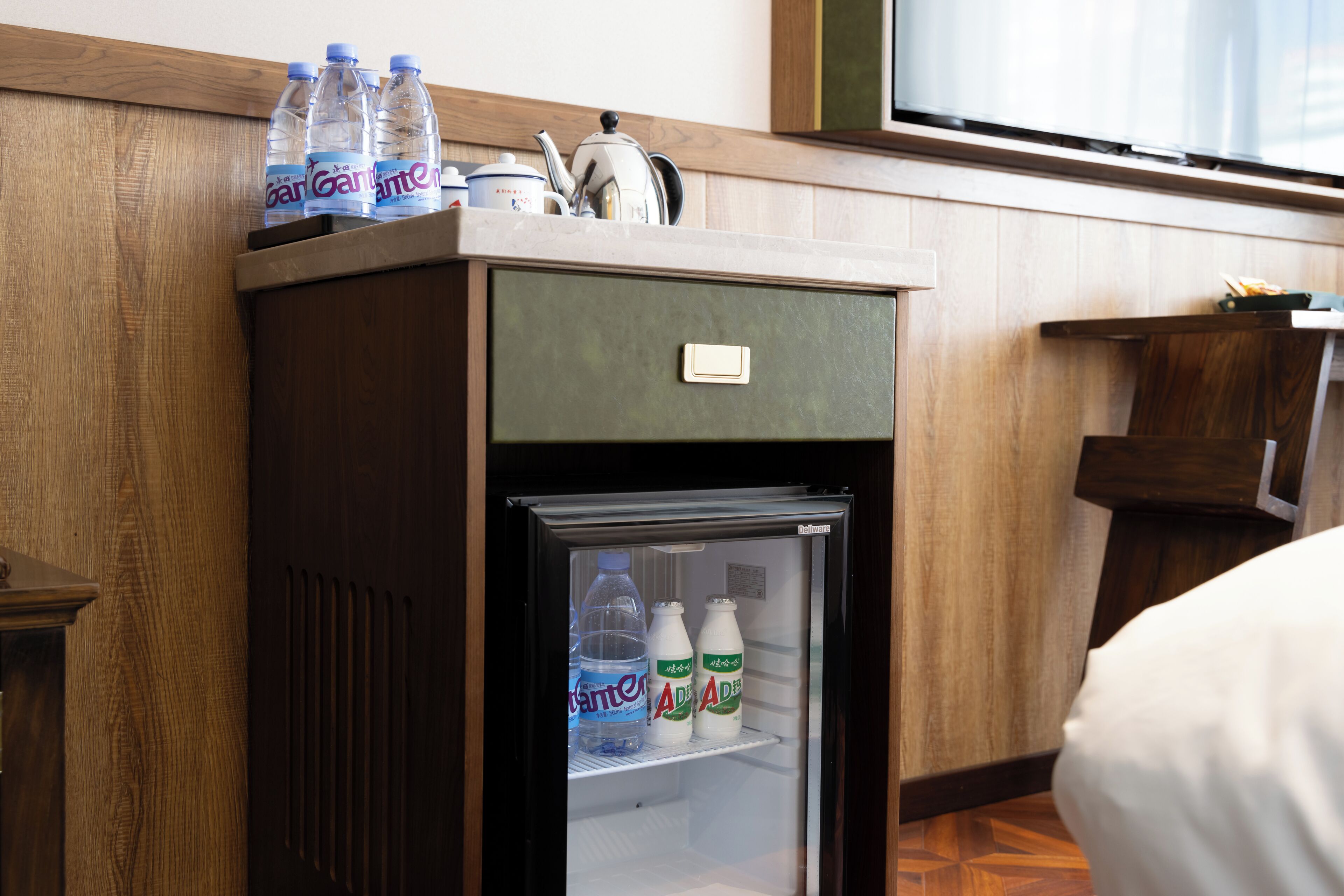 Un refrigerador compacto con botellas de agua y cartones de leche en su interior, ubicado en una habitación de hotel con paneles de madera.