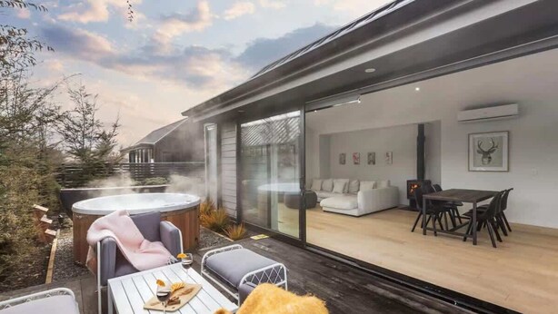 Une terrasse extérieure moderne dotée d’un jacuzzi, de coins salon et d’un espace de vie clos par des baies vitrées, comprenant un canapé et une table à manger.