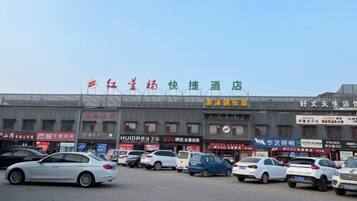 Un hôtel avec plusieurs boutiques donnant sur la rue et un parking où sont garées plusieurs voitures.