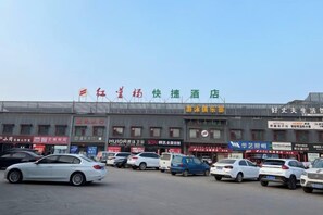 Un hôtel avec plusieurs boutiques donnant sur la rue et un parking où sont garées plusieurs voitures.