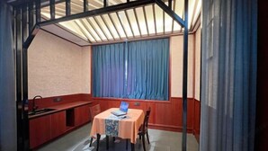A room with a dining table, chairs, a laptop, a window with curtains, and a kitchen area with a sink and cabinets. - HongxingyangExpressHotel (Wuxiang)