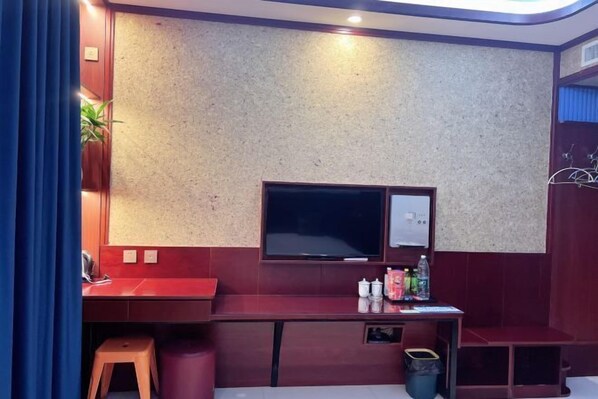 Quarto com escrivaninha vermelha, televisão e um banquinho pequeno.
