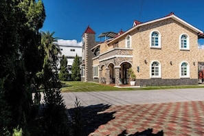 Un edificio de piedra grande con una torre, ventanas de arco y un camino pavimentado.