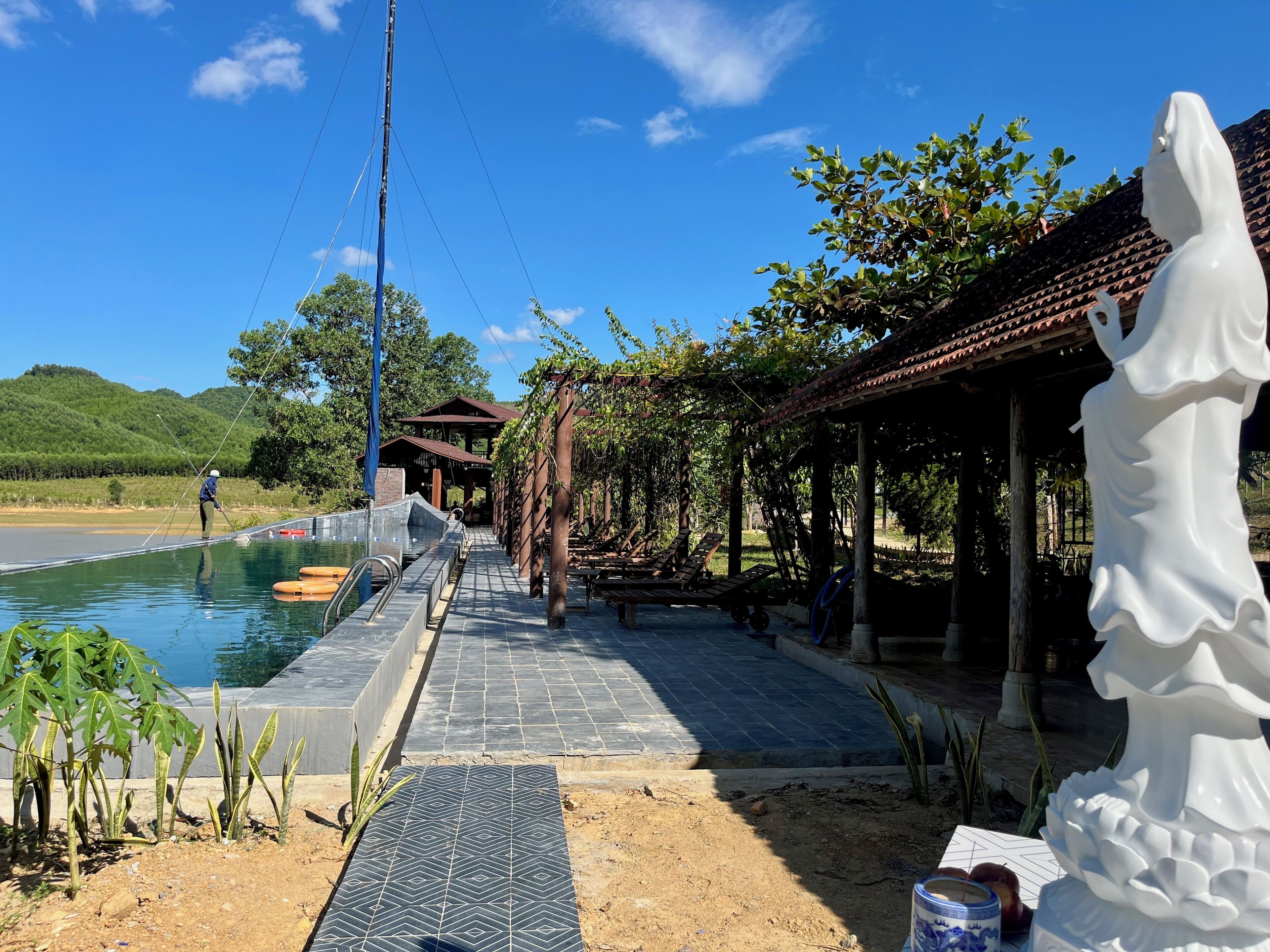 A pool area with a pergola, a statue, and a person fishing.