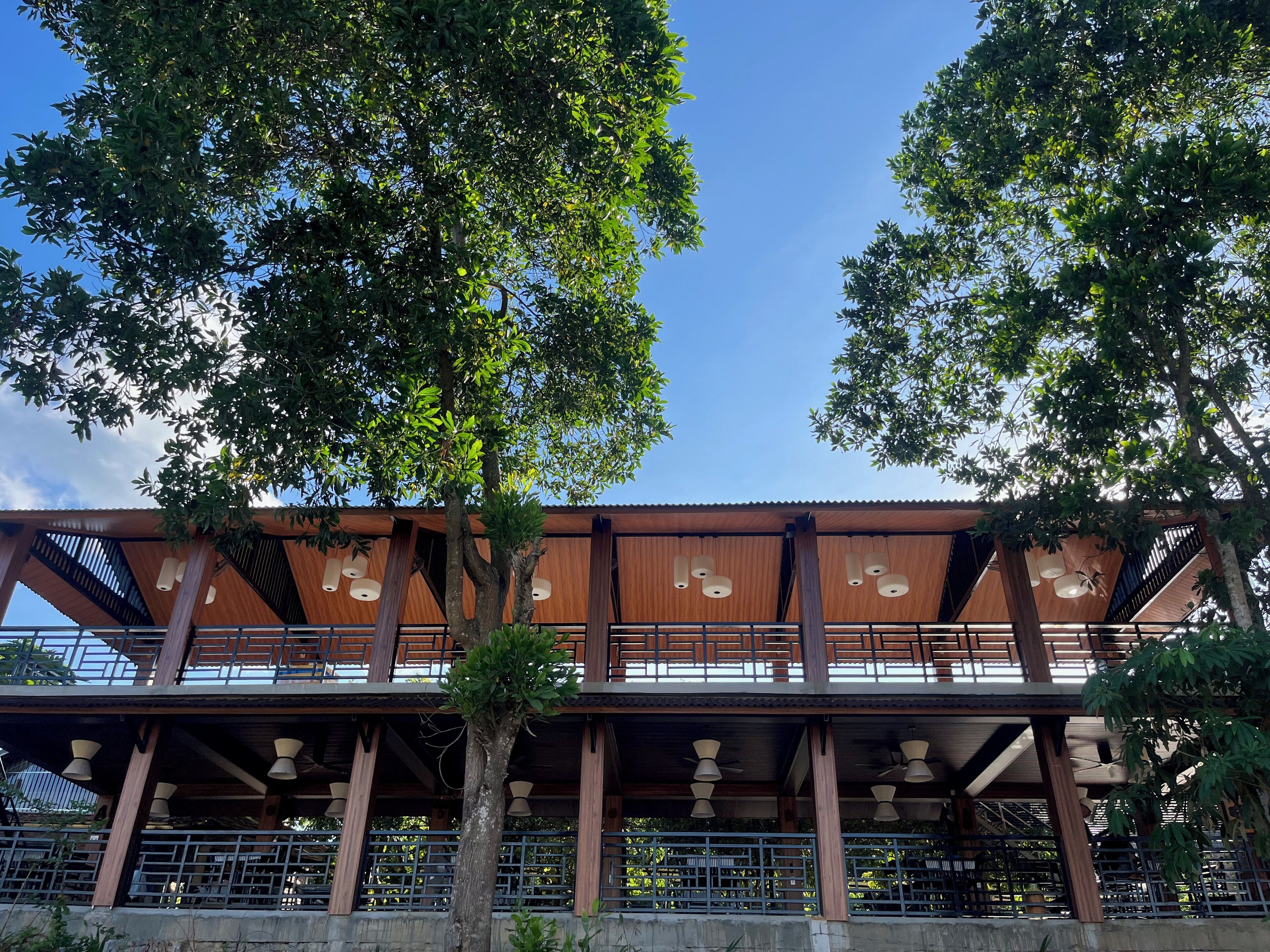 Um edifício moderno com fachada de madeira, grandes janelas e uma área externa coberta com assentos.