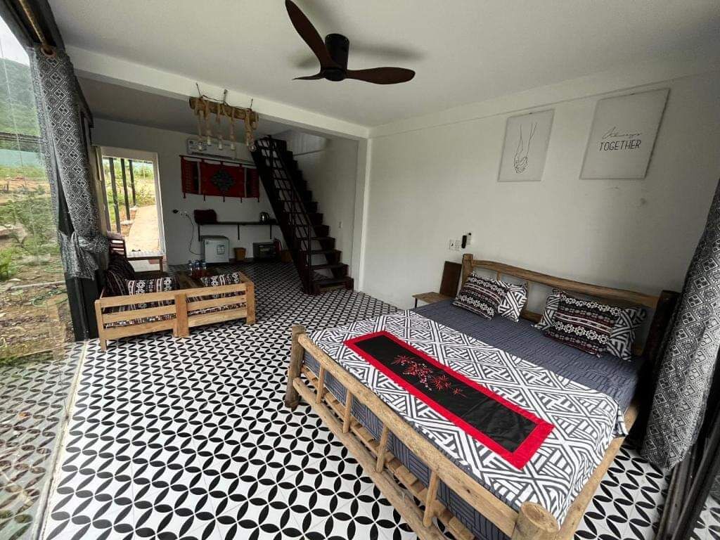 A bedroom with a patterned floor, a bed with a red runner, a ceiling fan, and a staircase leading to a kitchen.