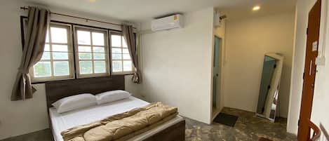 A bedroom with a bed, a window with curtains, an air conditioning unit, and a small table with a tissue box.