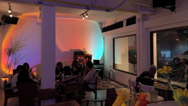 A restaurant with tables and chairs, a large window, and a plant. - cumpun hostel (Chiang Mai)