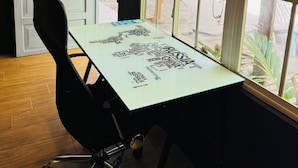 A room with a table displaying a world map, a black office chair, a white door, and a window with a view of the outside.