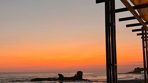 A sunset view from a covered walkway overlooking the beach, with a 'Surf City' sign visible.