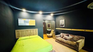 A room with a bed, a sofa, a wooden headboard, and artwork on the walls.