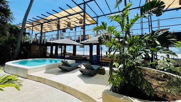 A pool area with lounge chairs, a pergola with a canopy, and tropical plants.