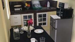 Una cocina compacta con una mesa de comedor para dos personas, con mantel negro, platos blancos, cubiertos y un florero con flores.