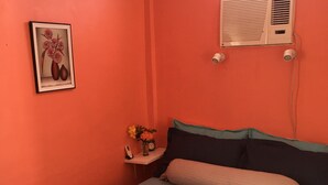Una habitación con una cama, una mesita de noche con un florero y un cuadro en la pared, además de un equipo de aire acondicionado.