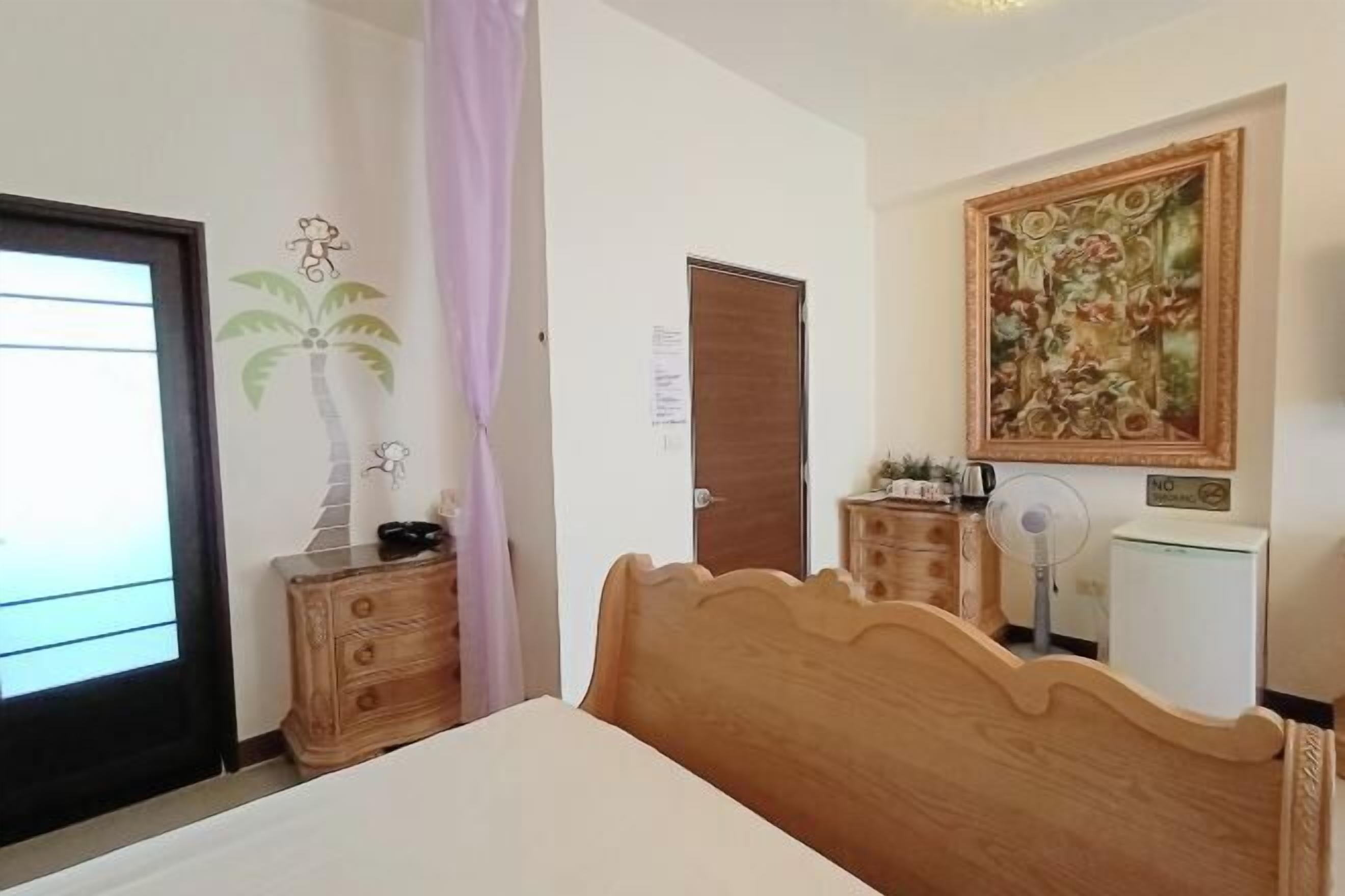 A bedroom with a wooden bed, a nightstand, a dresser, a painting on the wall, and a door with a sign.