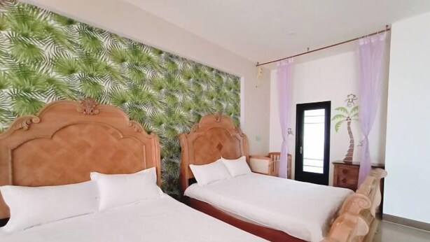 Una camera d'albergo con due letti, una parete decorata con un motivo a foglia tropicale e una testiera in legno.
