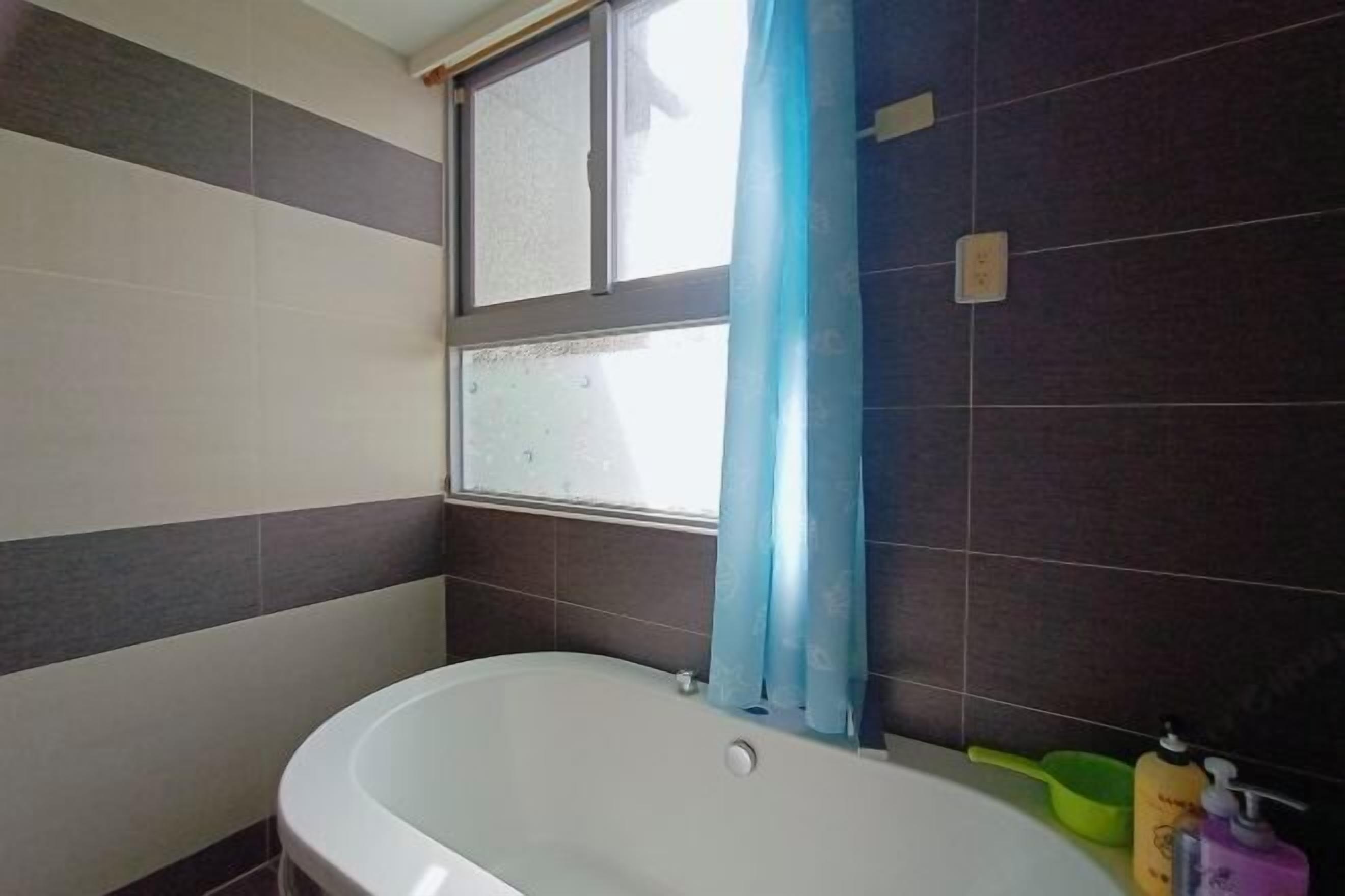 A bathroom with a bathtub, a window with a curtain, and a green basin.