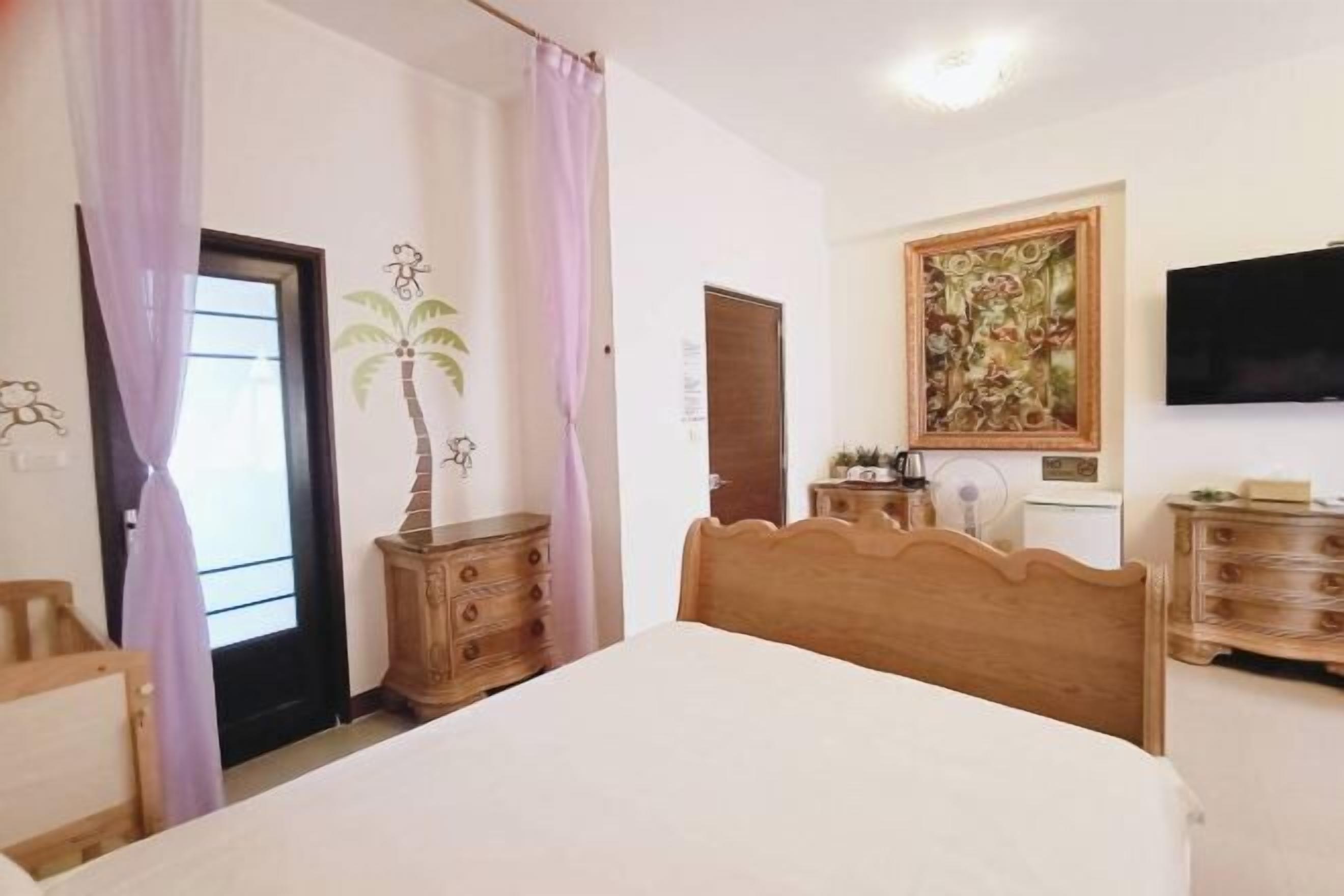 A bedroom with a bed, wooden dresser, a painting on the wall, and a television.