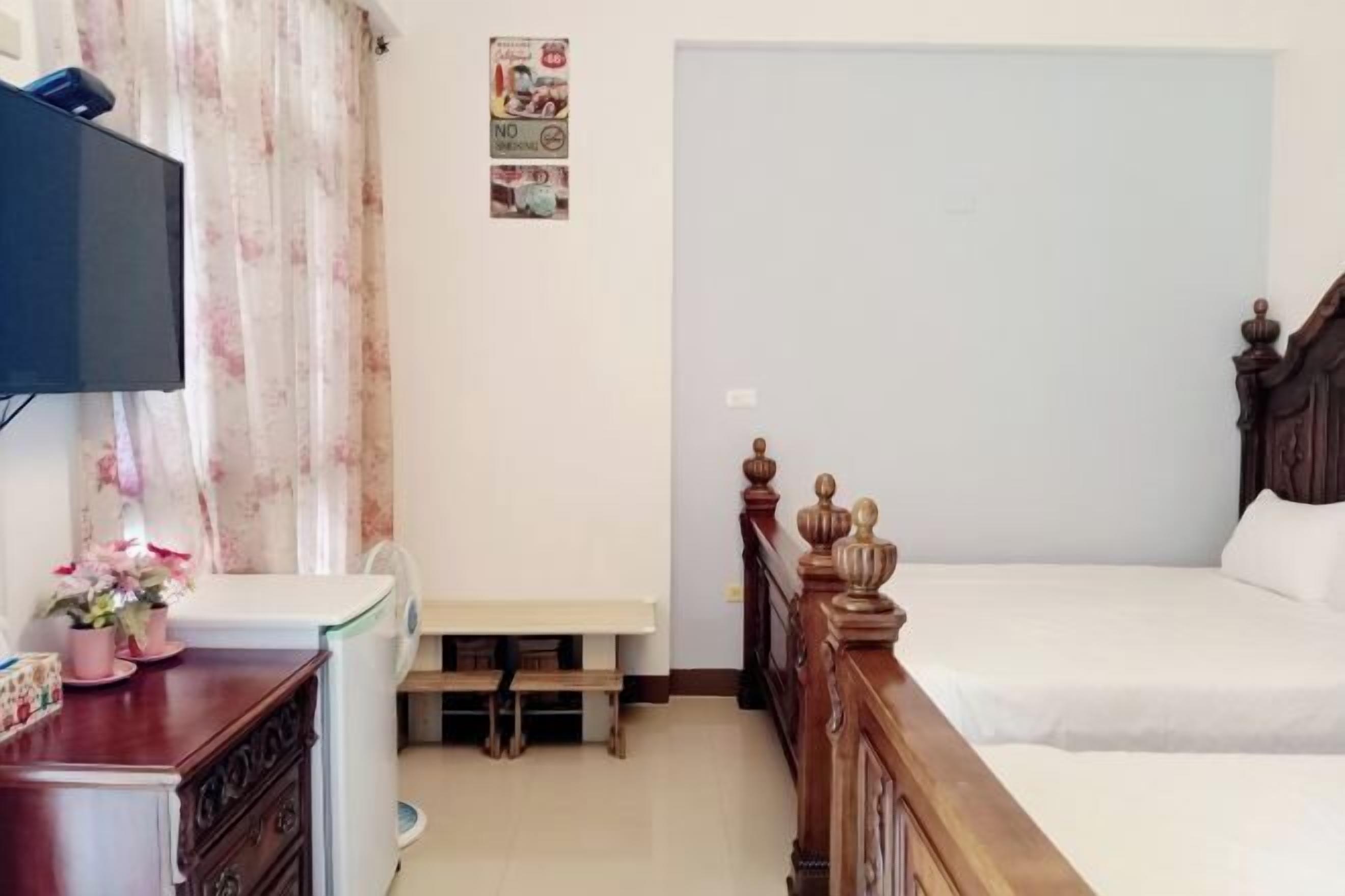 A bedroom with a wooden bed, a desk with a chair, a television, and a small table with a flower arrangement.