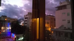 Una vista attraverso una finestra al crepuscolo, con edifici sullo sfondo e un cielo nuvoloso.