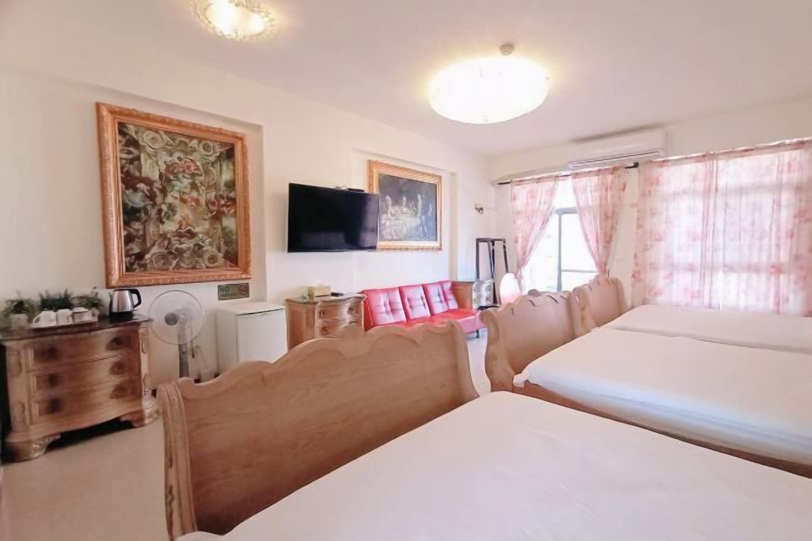 Habitación de hotel con dos camas, un televisor, un aparador de madera, un sofá rojo y obras de arte en las paredes.