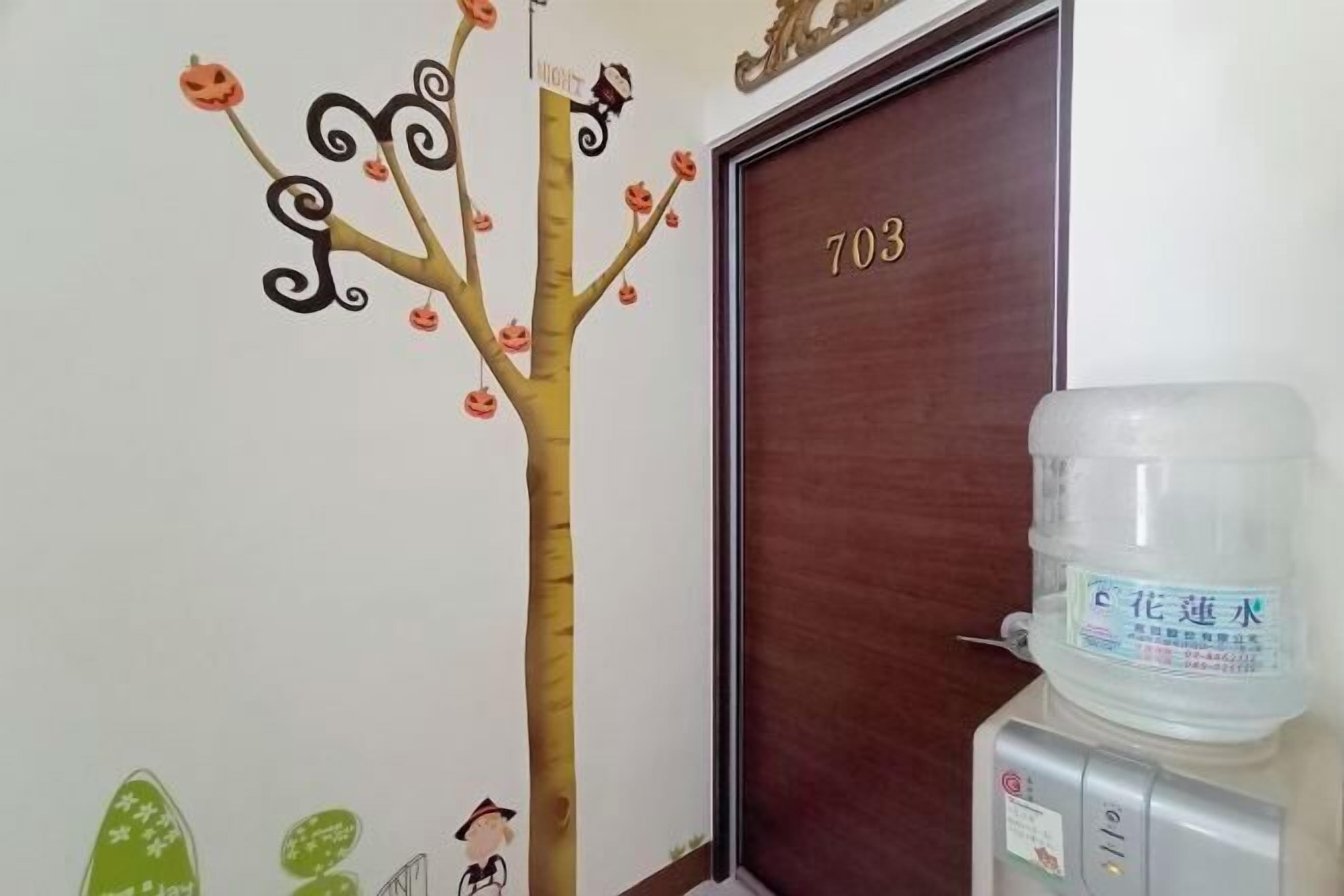 A room with a door labeled '703', a water dispenser, and a wall decal of a tree with pumpkins.