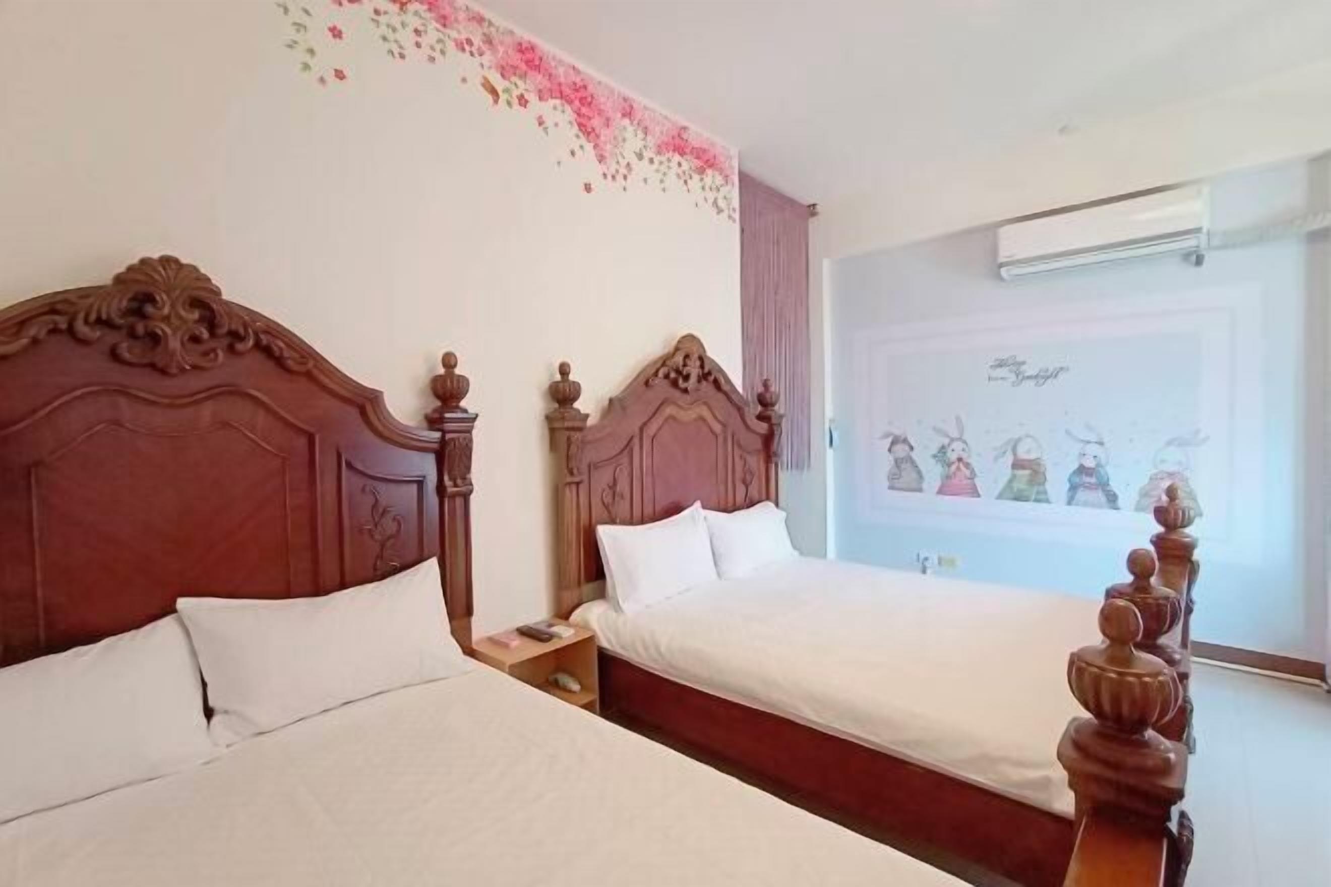 Two wooden beds with white linens in a room with a floral wall decal and a poster of cartoon characters.