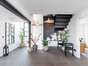 Experience the open-plan living area with a high ceiling and exposed beams, featuring a central staircase and natural ambiance.