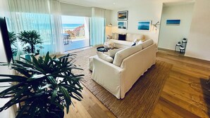 A modern living room with a white sofa, a coffee table, and a view of the ocean through large windows. - Slice Of Paradise - Direct Resort & Beach Access Apart - 3 Bed - Ocean Views (Cabarita Beach)