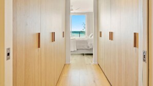 A hallway with wooden doors leading to a bedroom with a bed and a view of the ocean. - Slice Of Paradise - Direct Resort & Beach Access Apart - 3 Bed - Ocean Views (Cabarita Beach)