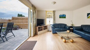 Sala de estar com televisão, sofás, mesa de centro e vista para o exterior.